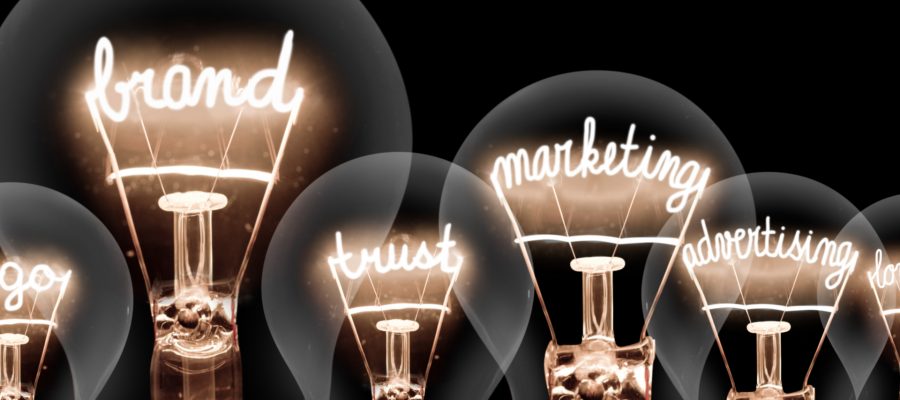 Photo of light bulbs with shining fibres in shape of BRAND concept related words isolated on black background